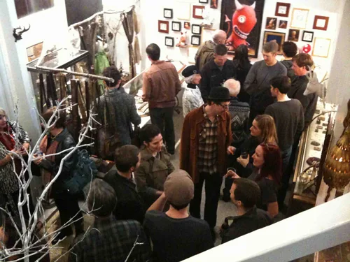 A lively crowd filling the Modern Relics gallery during the Yipe! 5 launch party, surrounded by Dylan Sisson's monster artwork.