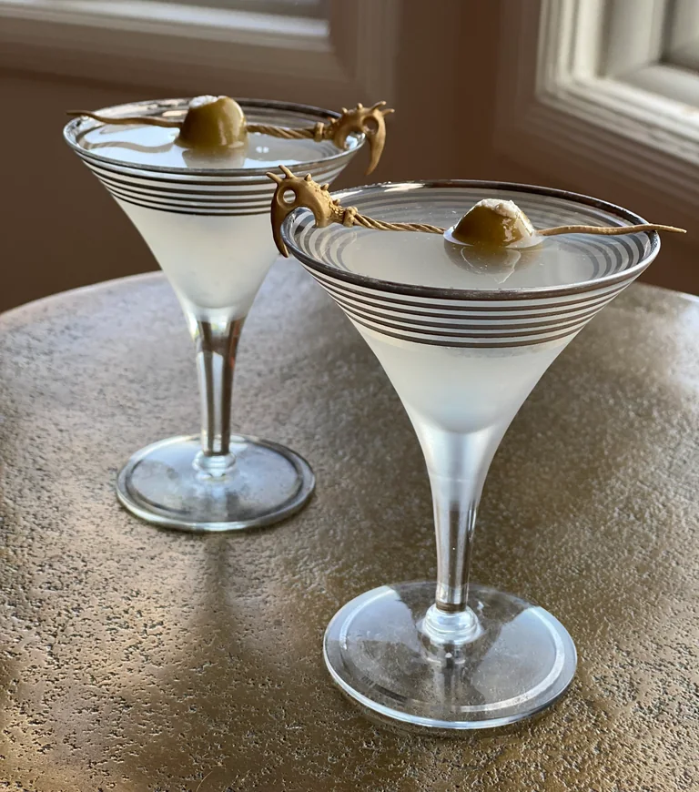 Early metal Dragon Pick prototypes resting across cocktail glasses.