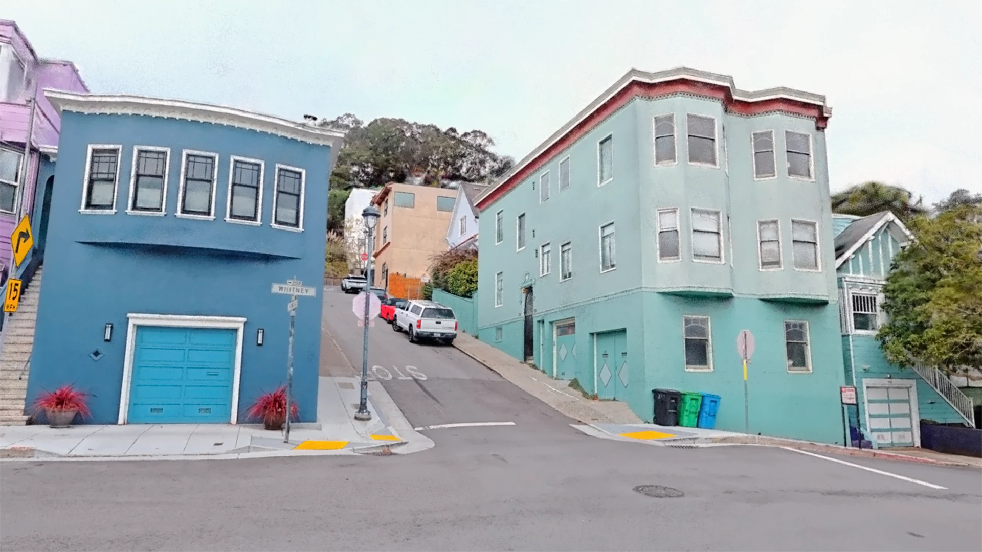Captured San Francisco street corner with blue and mint houses and cars parked uphill.