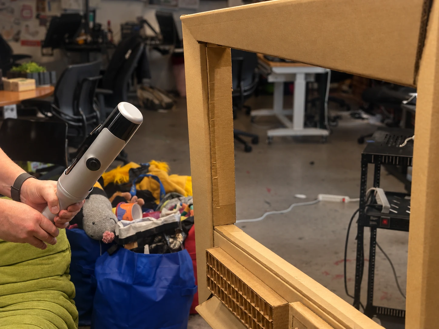 Hands holding the Kosmo camera beside the physical cardboard television in the Lab.