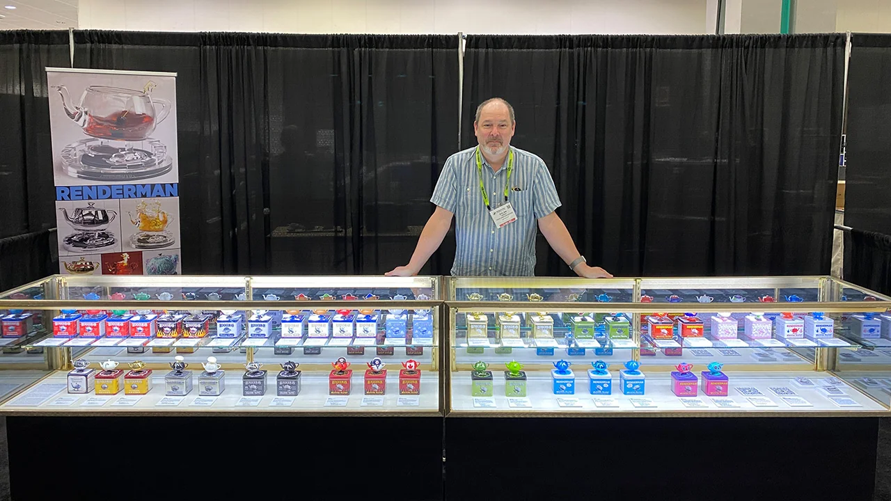 Dylan Sisson standing behind museum display cases filled with colorful RenderMan Walking Teapot editions.